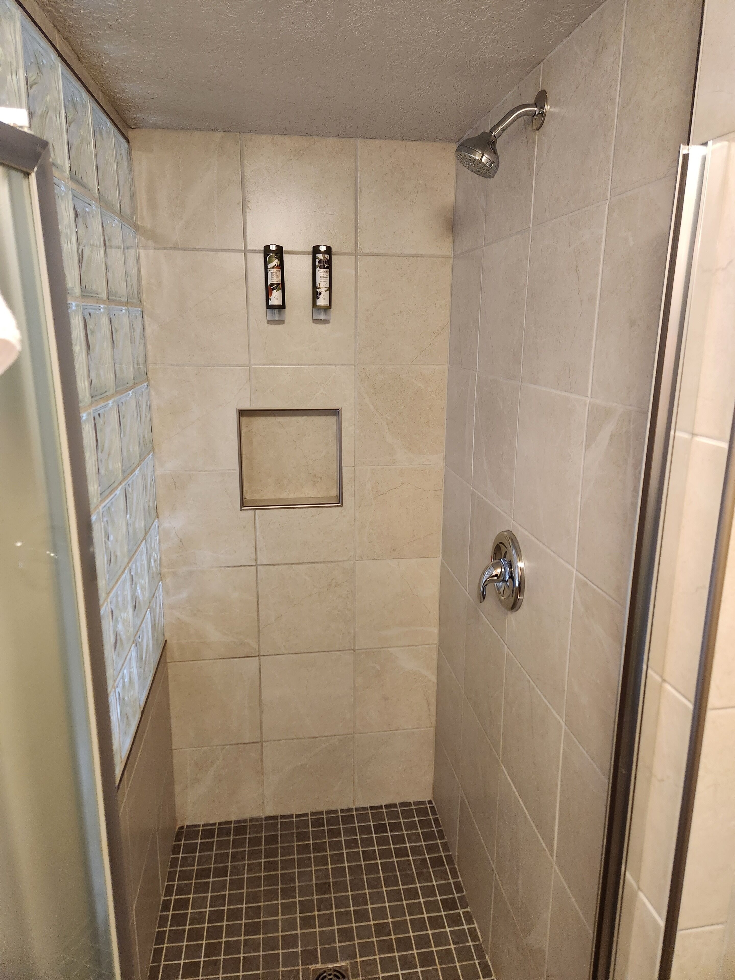 A small, tiled shower area with a showerhead and a wall-mounted soap dispenser.