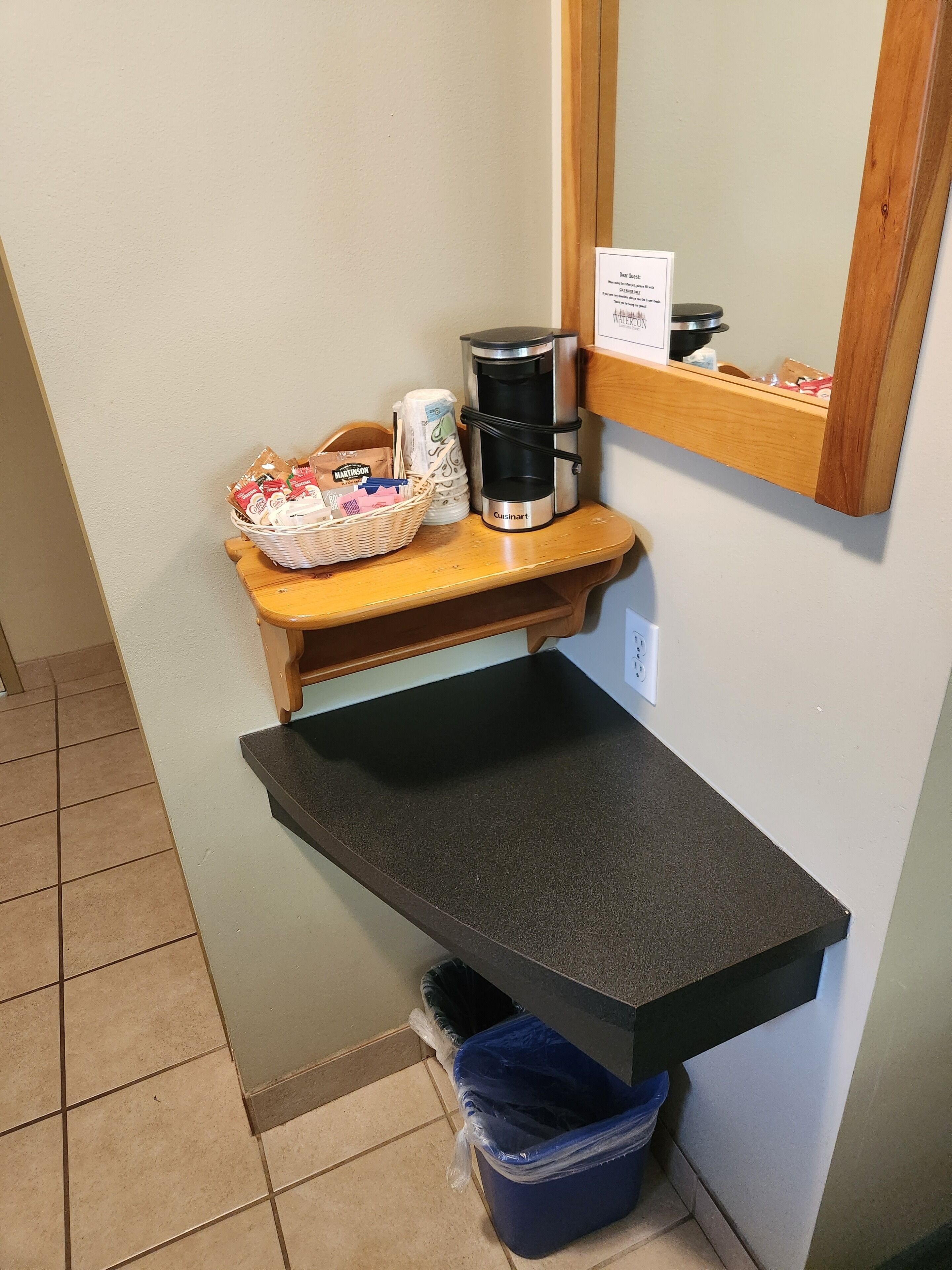 A kitchenette with a coffee maker, a basket of bread, and a trash bin.