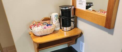 A kitchenette with a coffee maker, a basket of bread, and a trash bin.