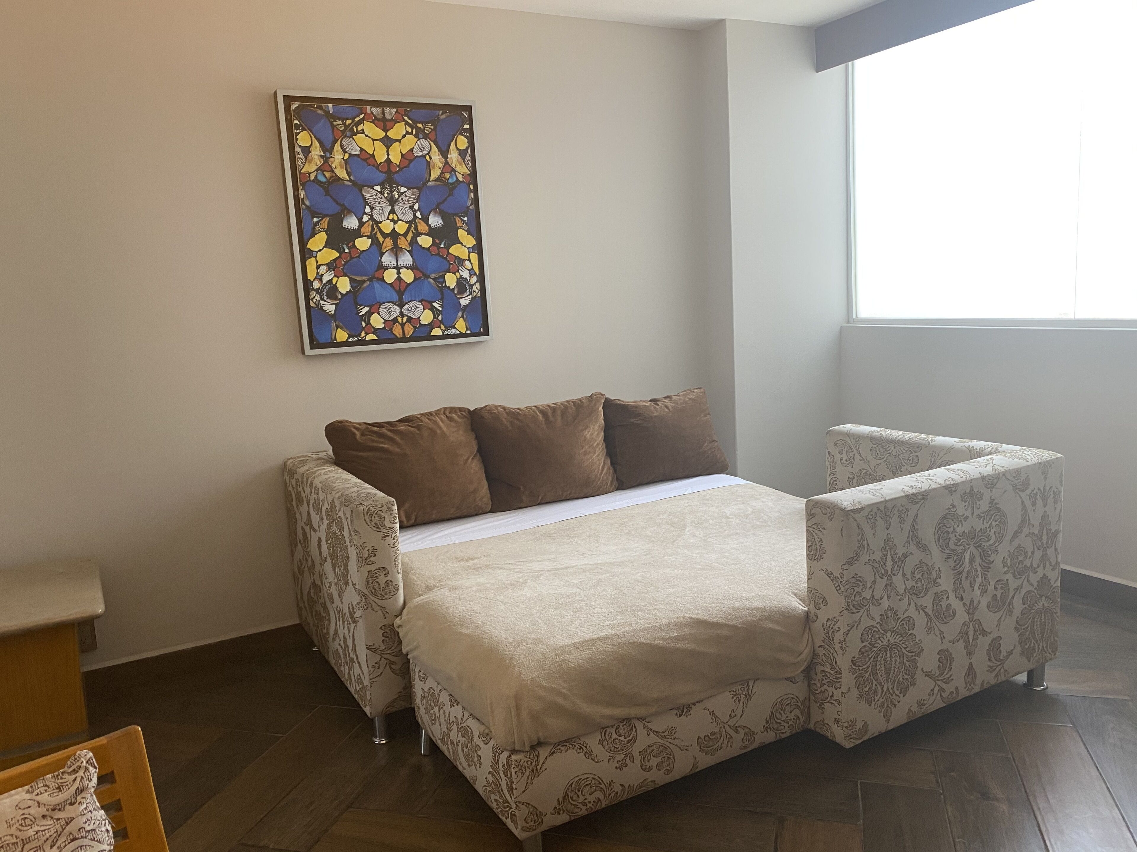 Un dormitorio con cama, una silla, una mesita y un ventanal.