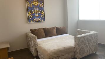 Un dormitorio con cama, una silla, una mesita y un ventanal.