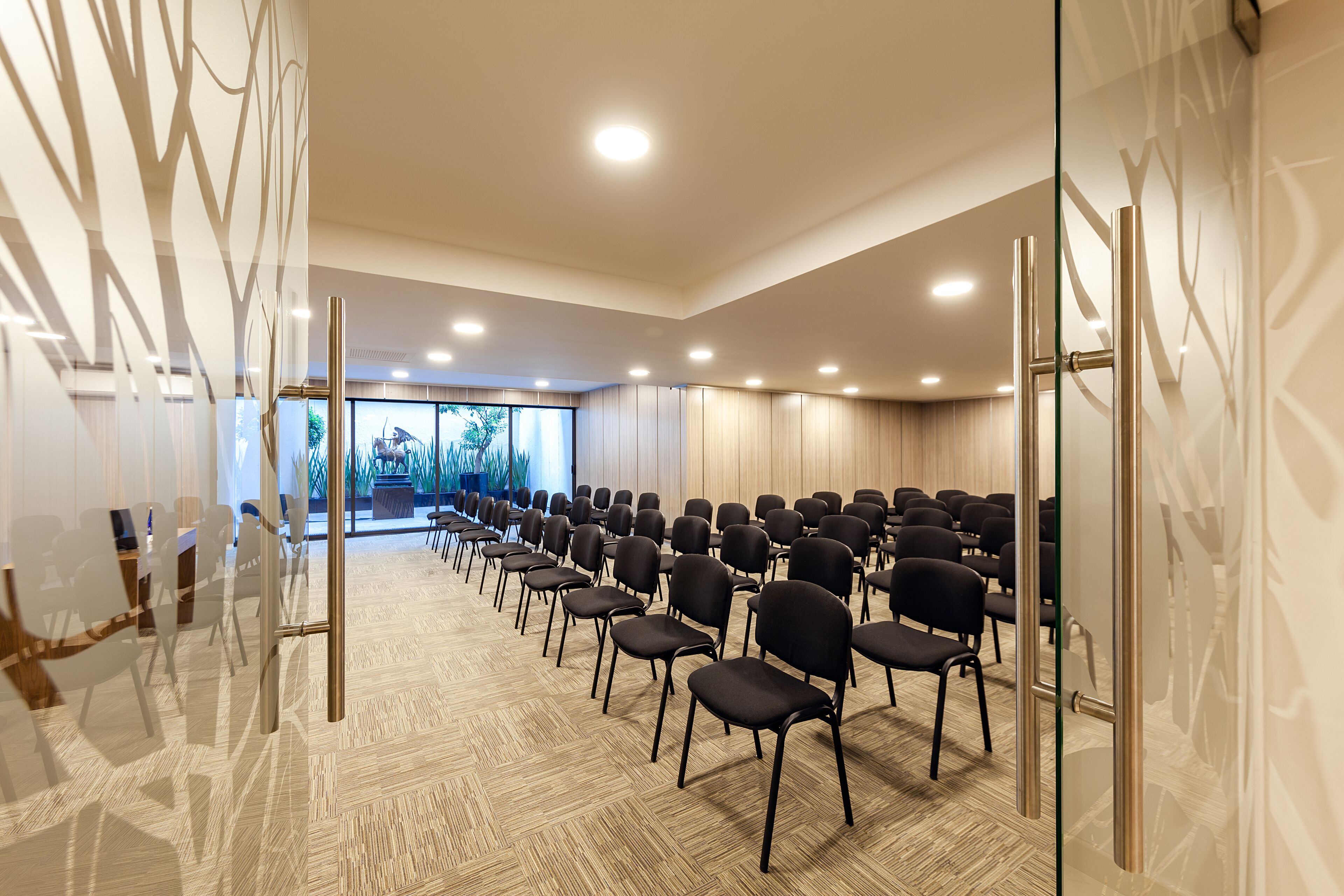 A conference room with rows of chairs, a glass partition, and a view of greenery outside.