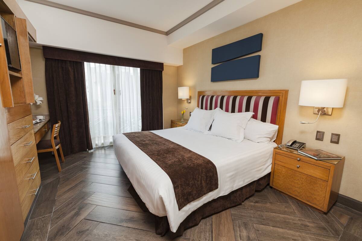 A hotel room with a large bed, wooden nightstand, desk, and chair.