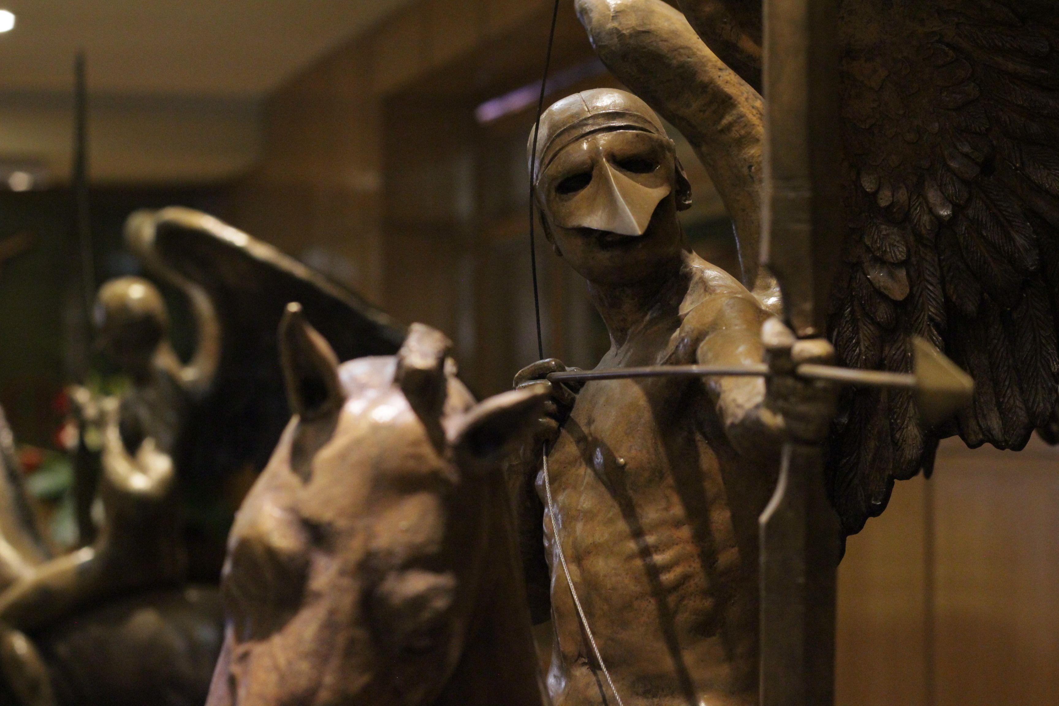 A sculpture of a figure with a mask and an arrow, likely part of a larger exhibit.