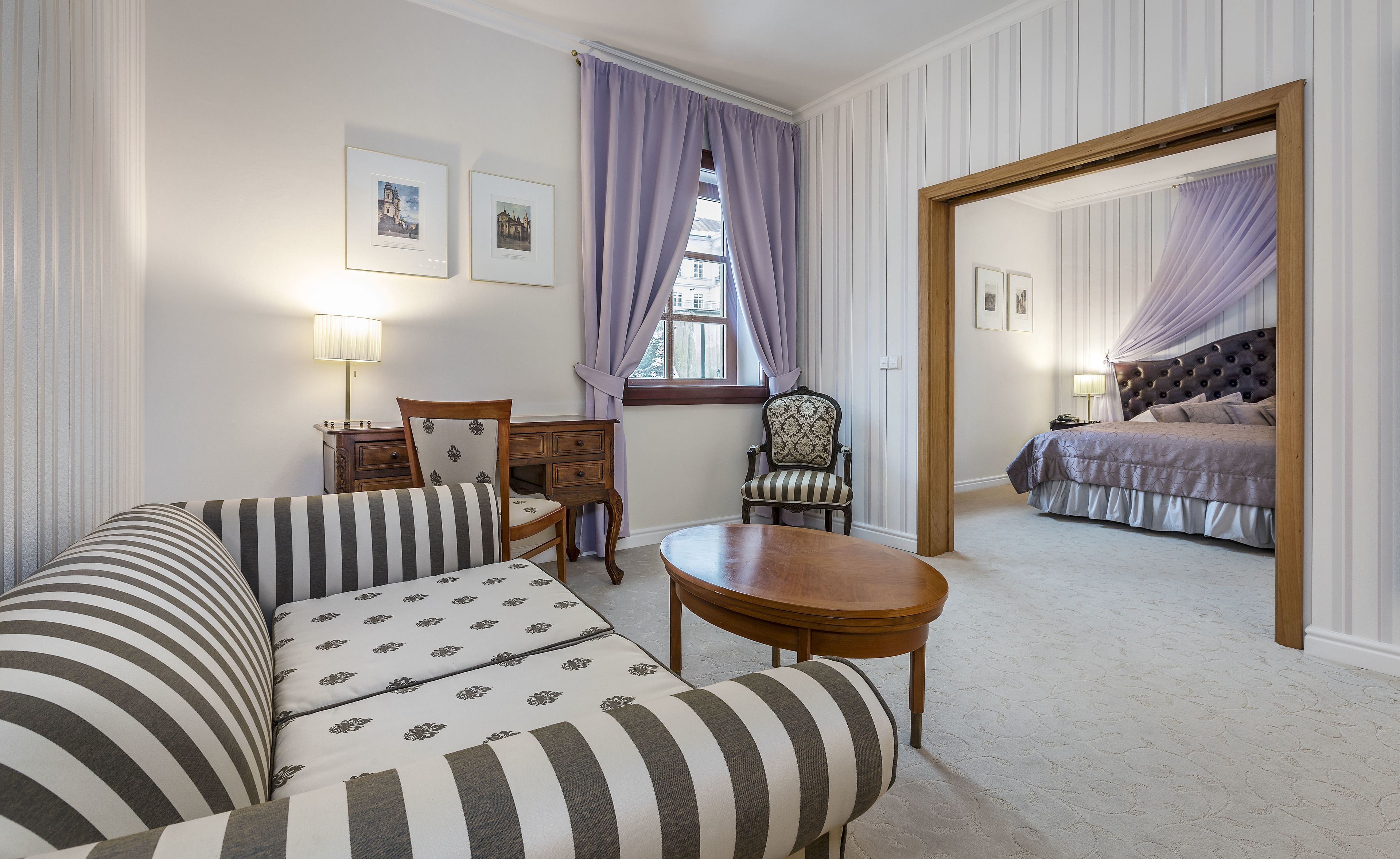 A hotel room with a striped sofa, a wooden chair, a round table, and a bed with a canopy.