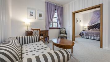 A hotel room with a striped sofa, a wooden chair, a round table, and a bed with a canopy.