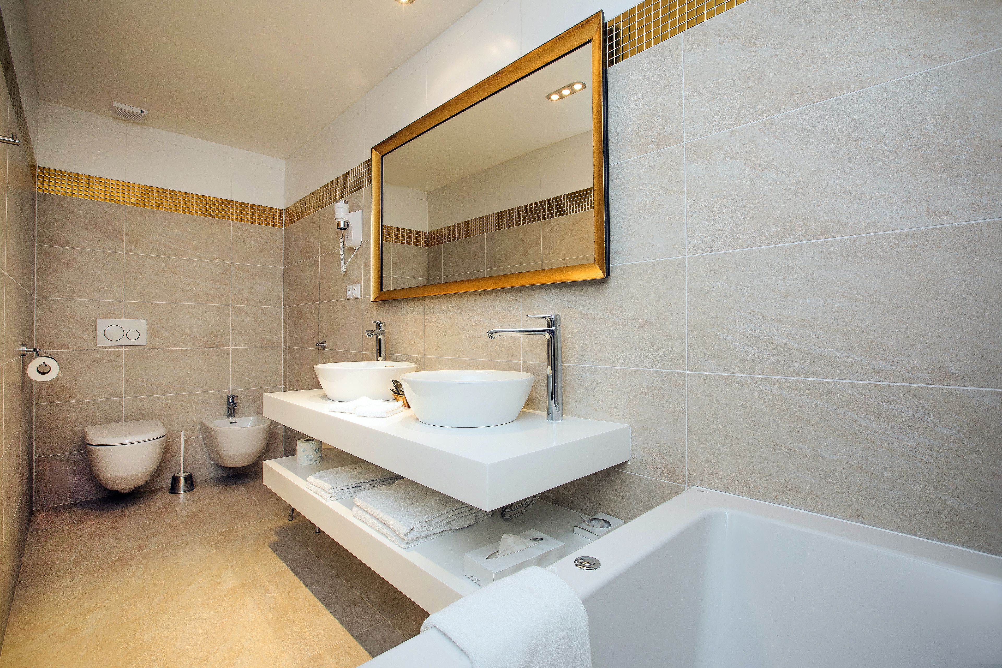 Un baño moderno con un espejo grande, dos lavamanos, un bidé y una bañera.