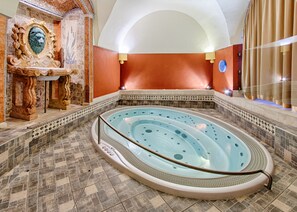 Un área de spa con un jacuzzi, decoración de pared elaborada y suelo de baldosas.