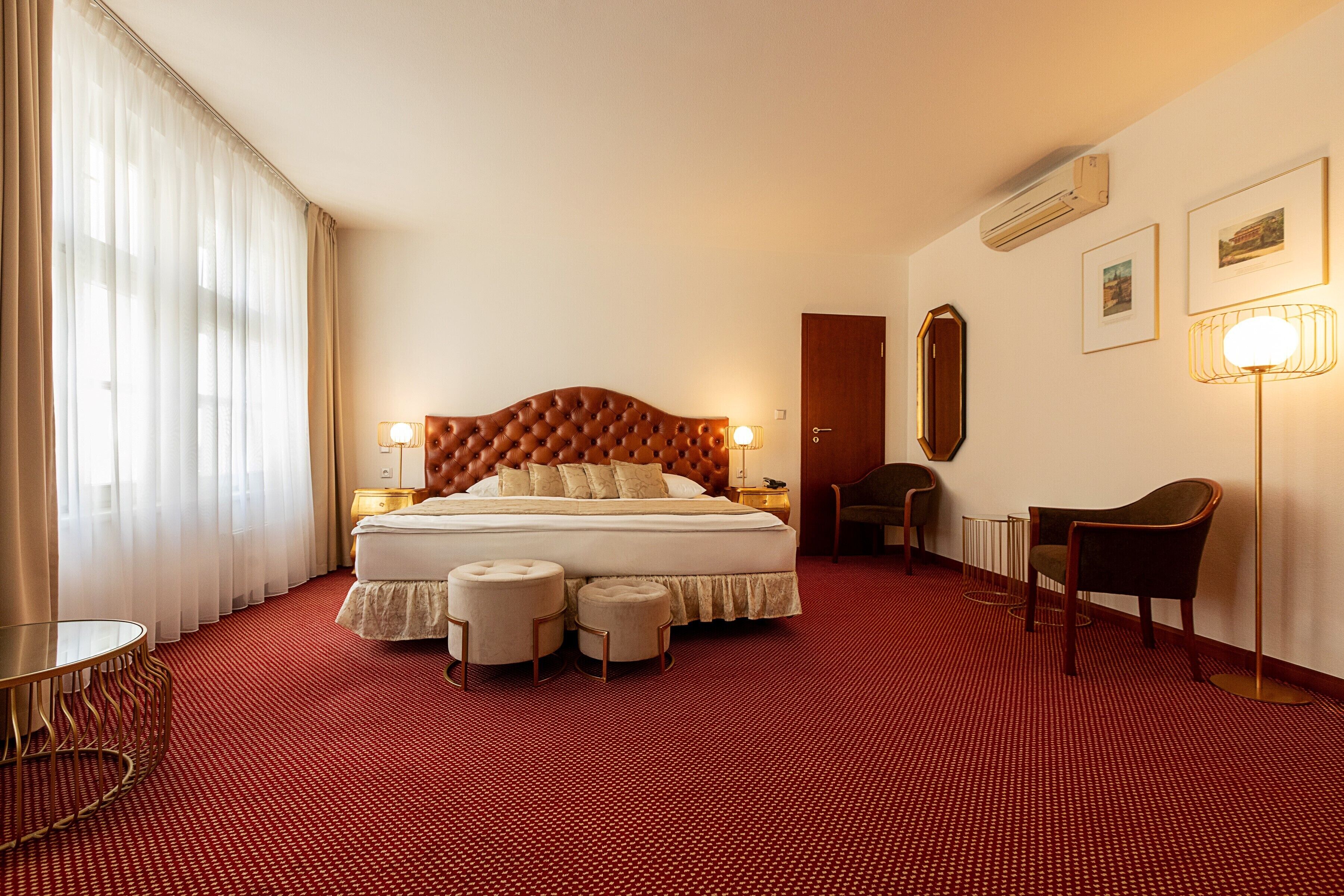 Een hotelkamer met een groot bed, twee nachtkastjes, een stoel, een ronde tafel en een rood tapijt.