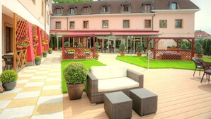 A spacious outdoor patio with wicker furniture, a checkered floor, and a building with a red awning in the background. - Hotel Hoffmeister (Prague)