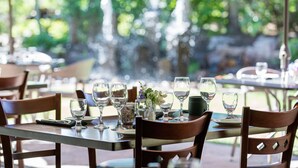 An outdoor dining area with tables set for two, featuring clear glassware and a small floral centerpiece. - Knob Hill Inn (Ketchum)