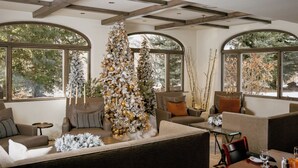 A modern living room with a large Christmas tree, comfortable seating, and large windows offering views of trees. - Knob Hill Inn (Ketchum)
