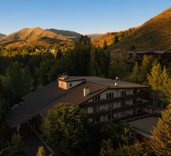 A multi-story building with a flat roof, surrounded by dense forest and mountains in the background.
