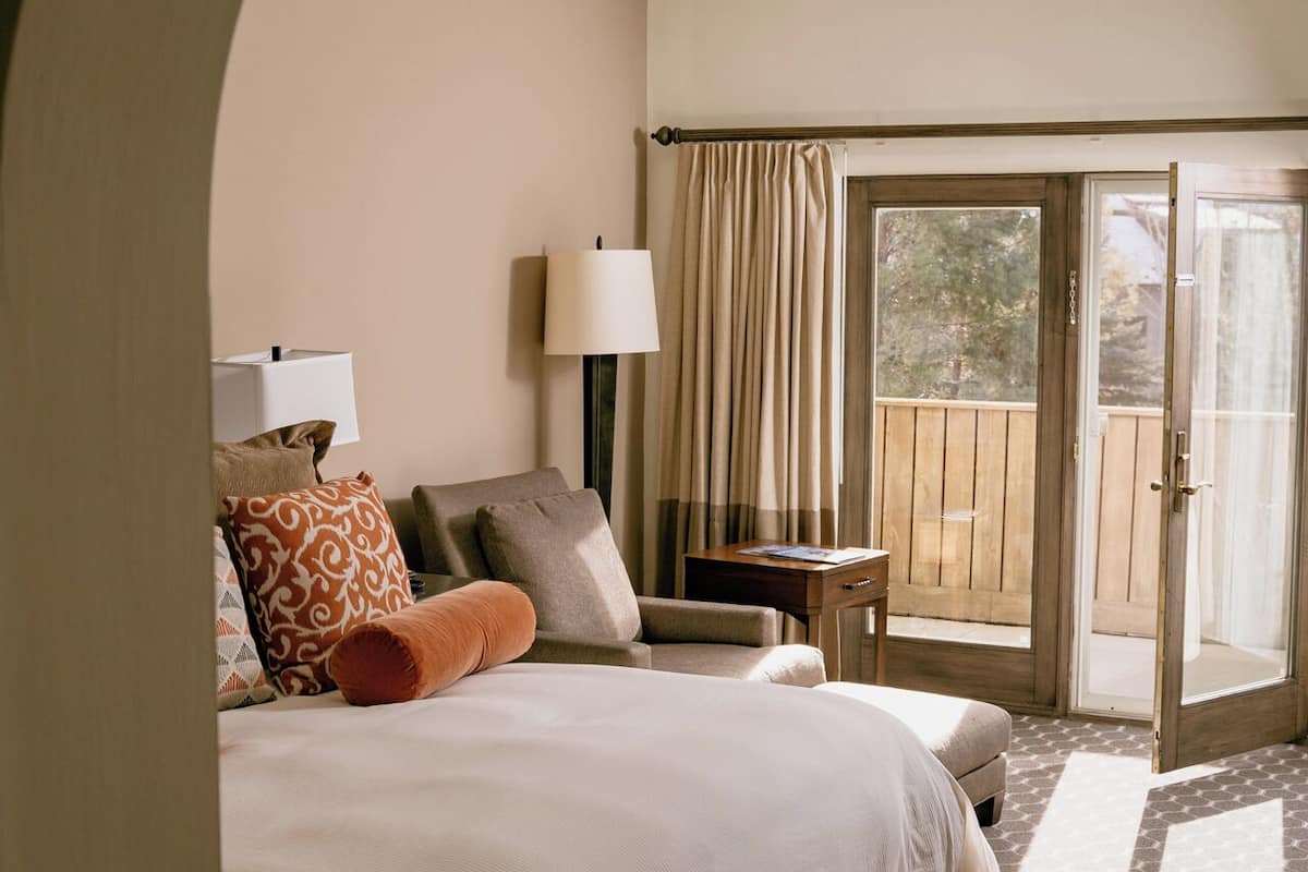 A bedroom with a large bed, a nightstand, a lamp, and a view of the outdoors through a sliding glass door.