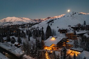 A snow-covered mountain town at dusk with illuminated buildings and a visible road.