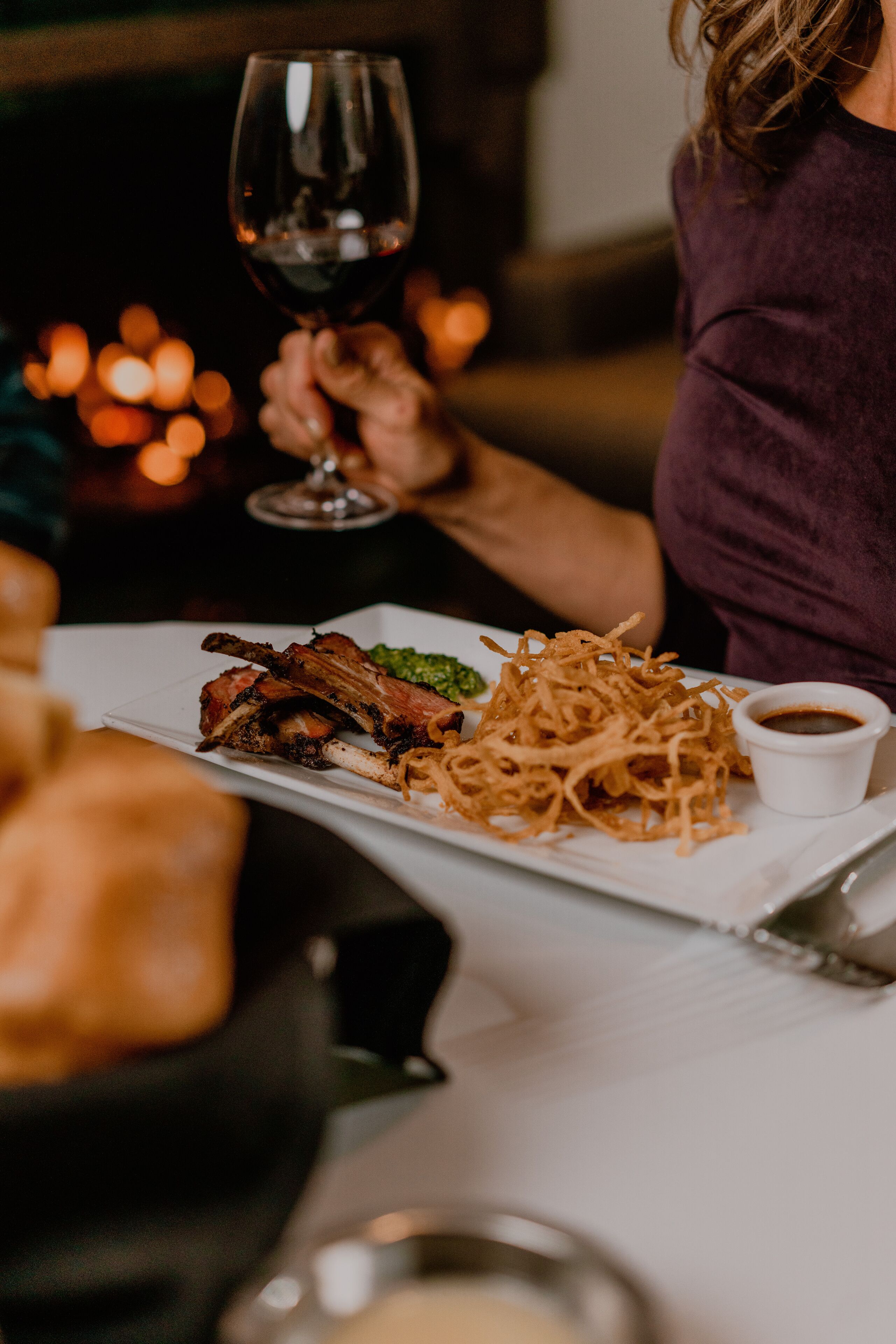 A dining table with a plate of food, a glass of red wine, and a candle in the background.