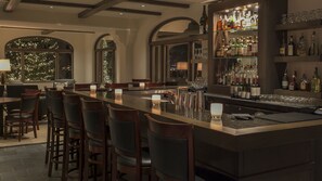 A bar area with a long counter, bar stools, and a variety of bottles and glasses on shelves.