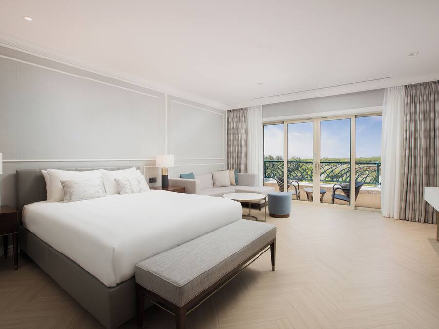 Quarto de hotel moderno com uma cama grande, área de estar e varanda com vista.