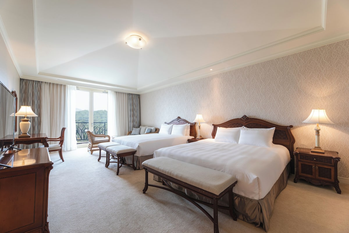 Une chambre d’hôtel avec deux lits, un bureau, une chaise et un balcon avec des rideaux.