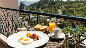 Enjoy a leisurely breakfast on the balcony with a view of the lush landscape, featuring a plate of eggs, bacon, and fresh fruit, accompanied by toast, coffee, and juice.