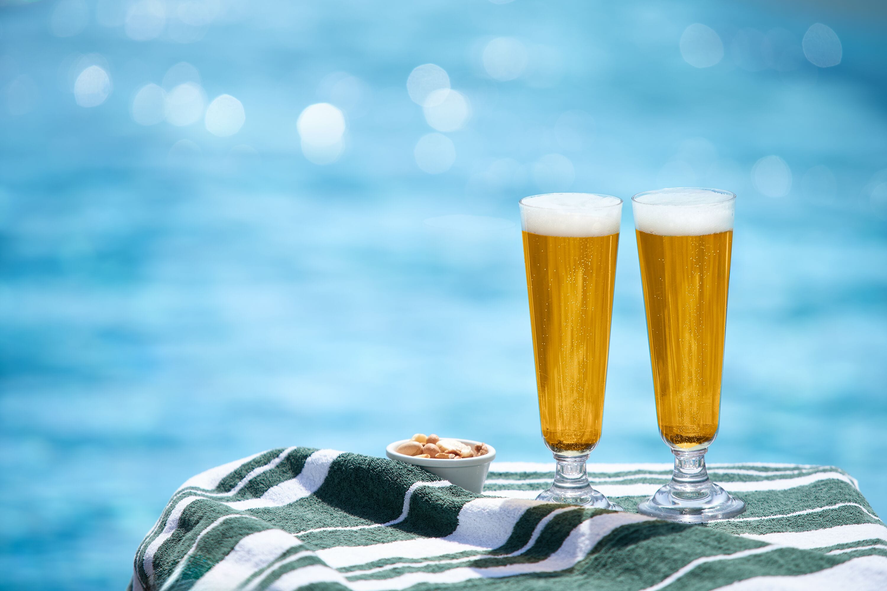 Duas cervejas sobre uma toalha listrada à beira da piscina.