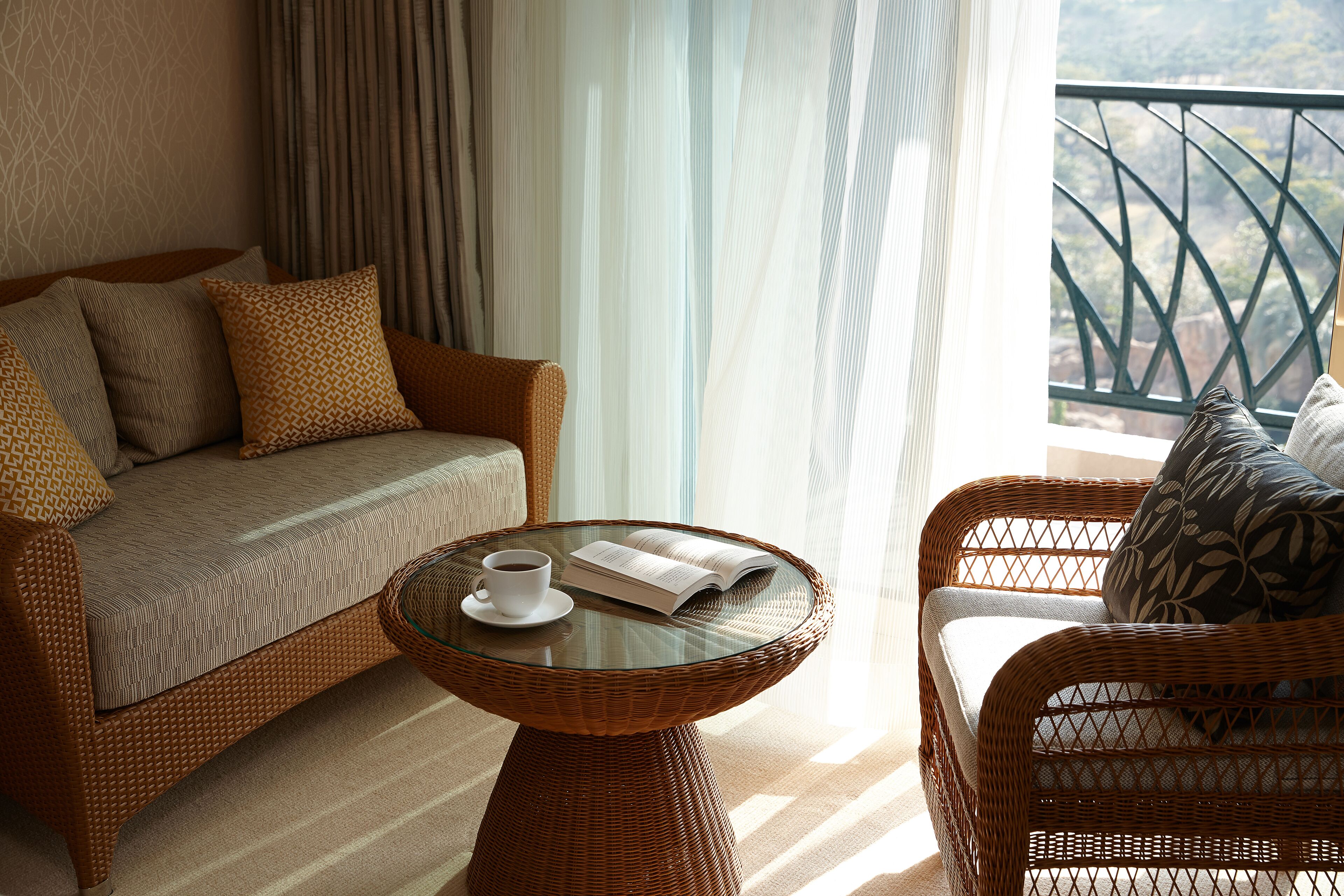 A cozy living area with a sofa, a wicker coffee table, and a view of a mountainous landscape through a balcony railing.