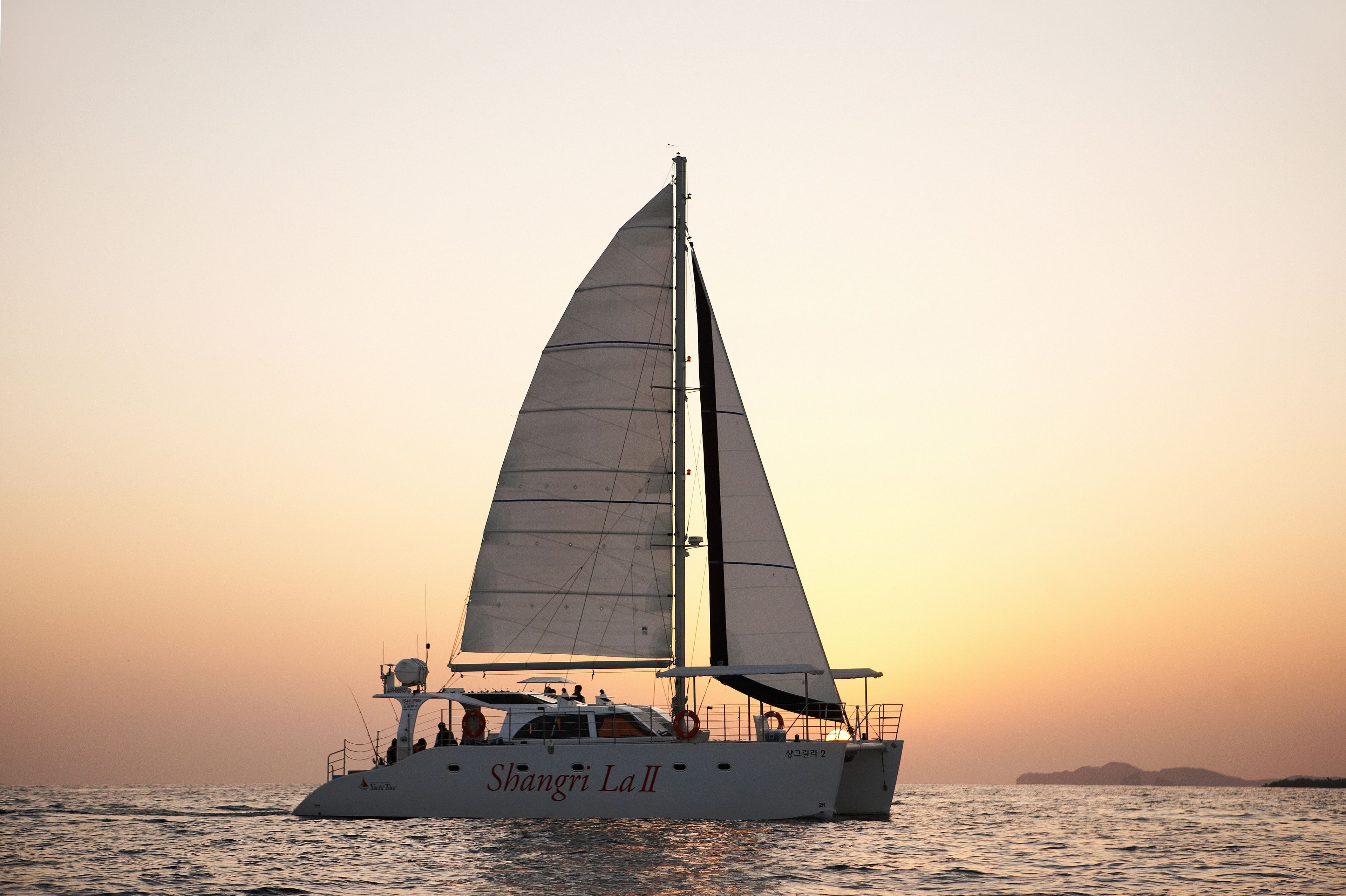 A sailboat named 'Shanghai La II' on calm waters during sunset.