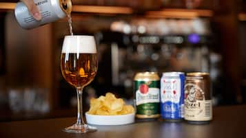 Ein Bierglas wird gerade mit Bier gefüllt, dazu liegen Chips und drei Bierdosen auf dem Tisch.