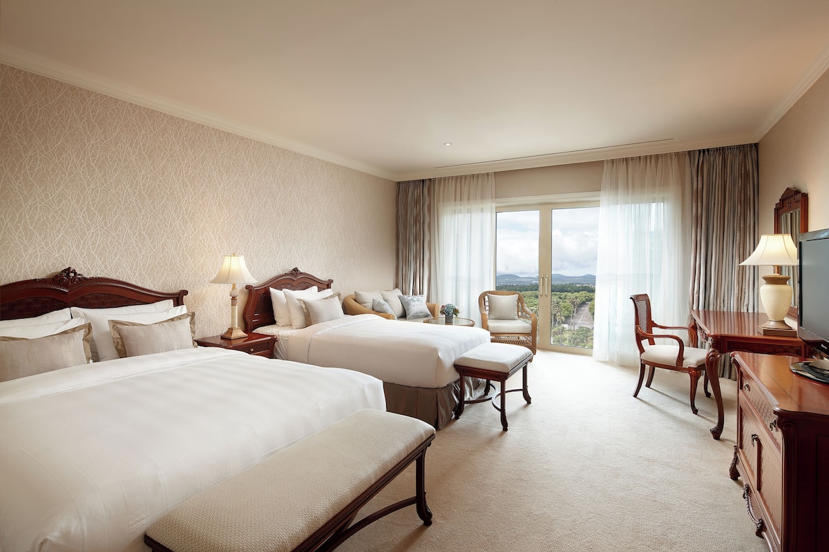 Une chambre d’hôtel avec deux lits, un bureau, une chaise et une grande fenêtre donnant sur un beau paysage.