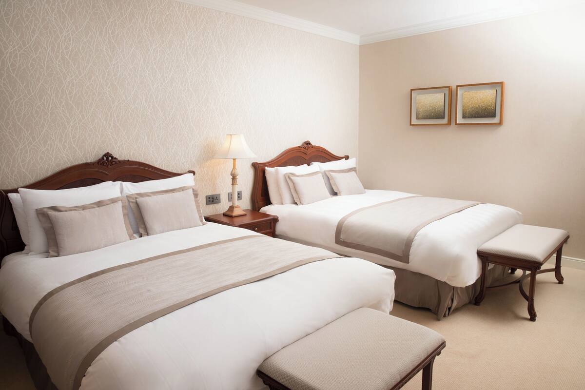Une chambre d’hôtel avec deux lits, une table de chevet, une lampe et deux tableaux encadrés au mur.