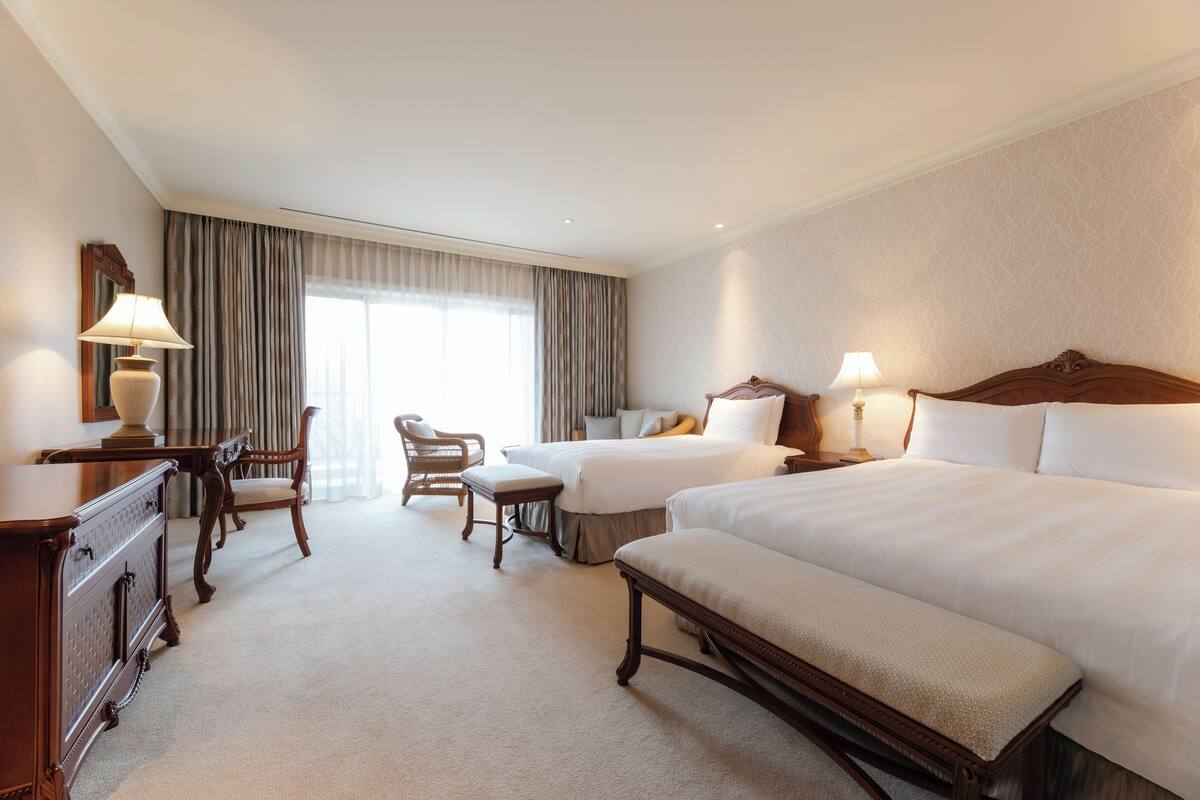 Une chambre d’hôtel avec deux lits, un bureau, une chaise et une lampe.