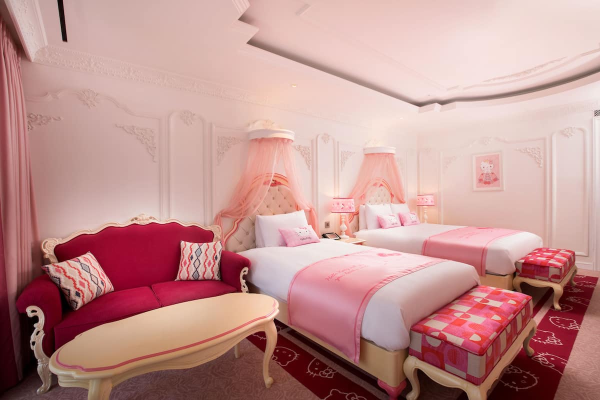 Une chambre à coucher décorée dans des tons de rose, avec deux lits, un canapé rouge et des poufs assortis.
