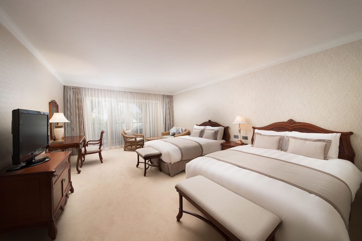 Une chambre d’hôtel avec deux lits, un bureau avec une télévision et une fenêtre avec des rideaux.