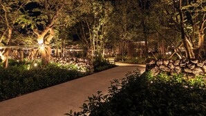 Un sendero en un jardín nocturno, con árboles y plantas iluminados por una luz tenue.