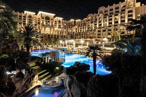 Un hotel con una piscina grande, palmeras y una formación rocosa.