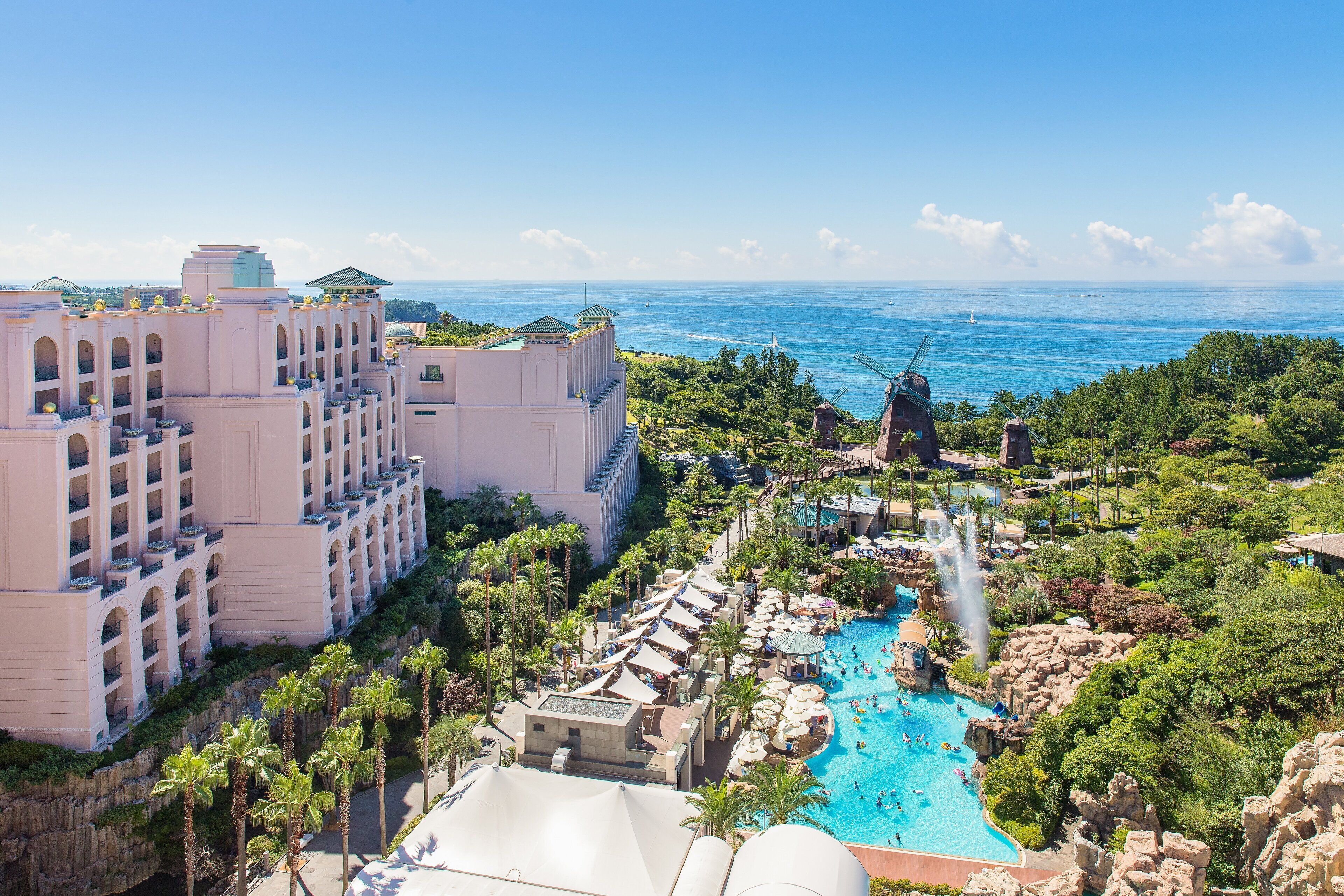 A resort with a large pool, palm trees, and a view of the ocean.