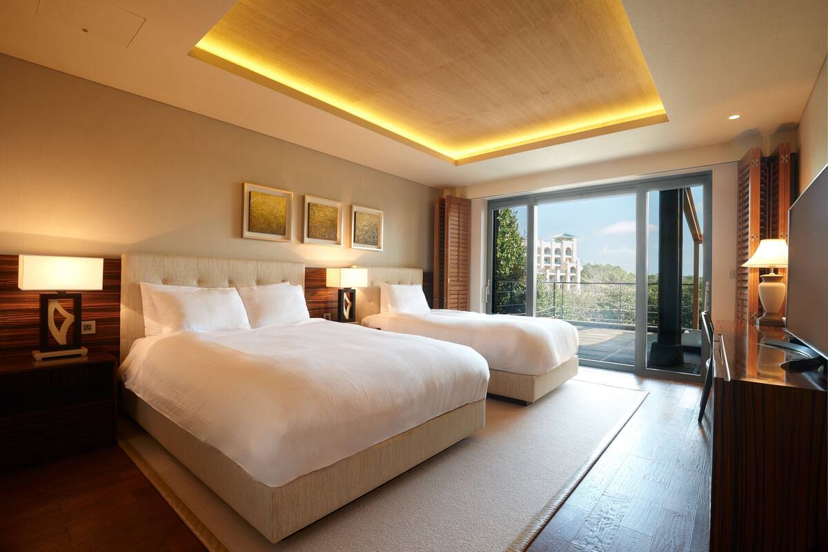 Une chambre d’hôtel avec deux lits, une grande fenêtre et une vue sur un immeuble.