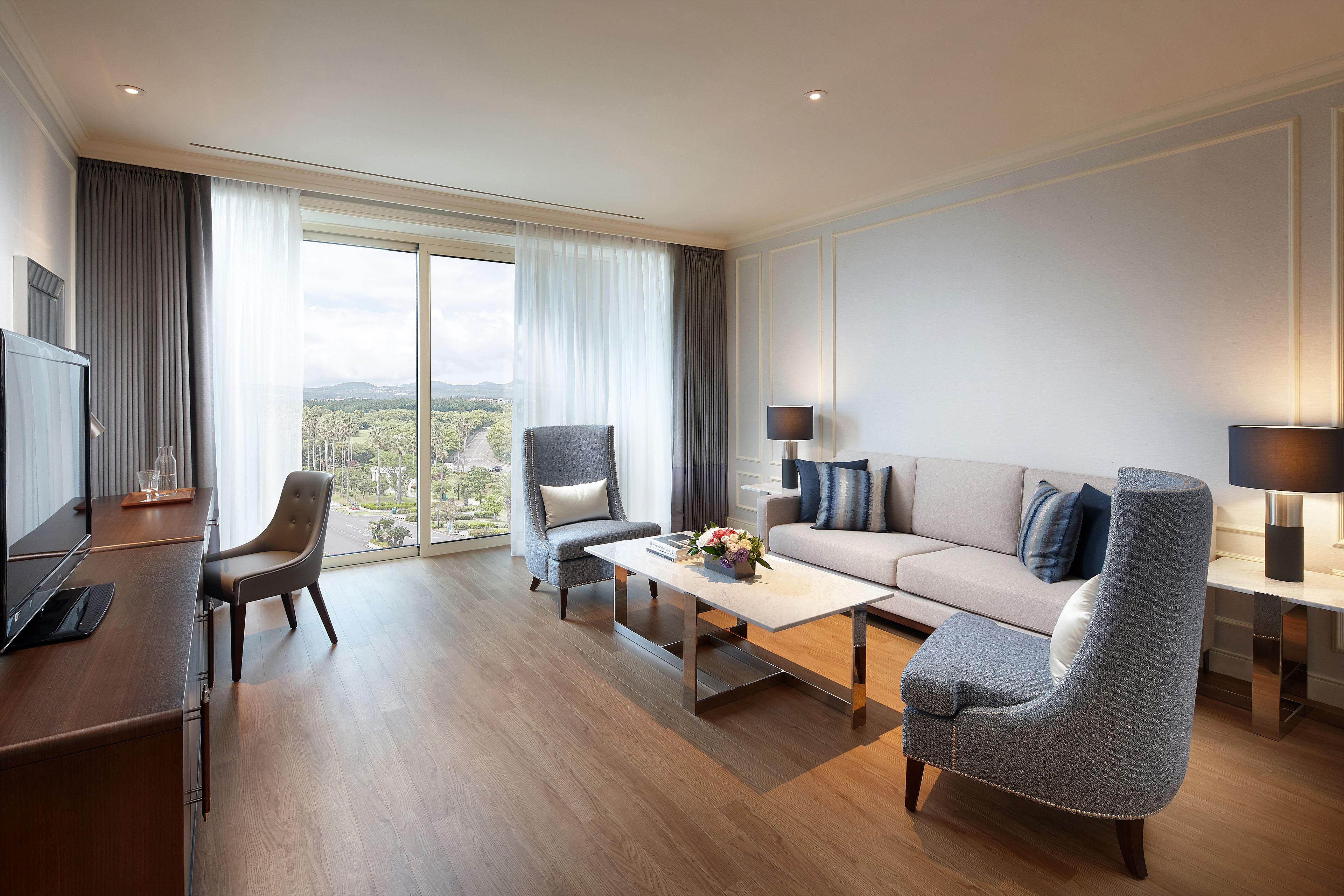 A modern living room with a sofa, two armchairs, a coffee table, and a TV.