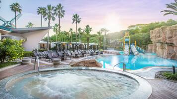 Relax by the pool surrounded by palm trees and a rock formation, with a hot tub and water slide nearby.