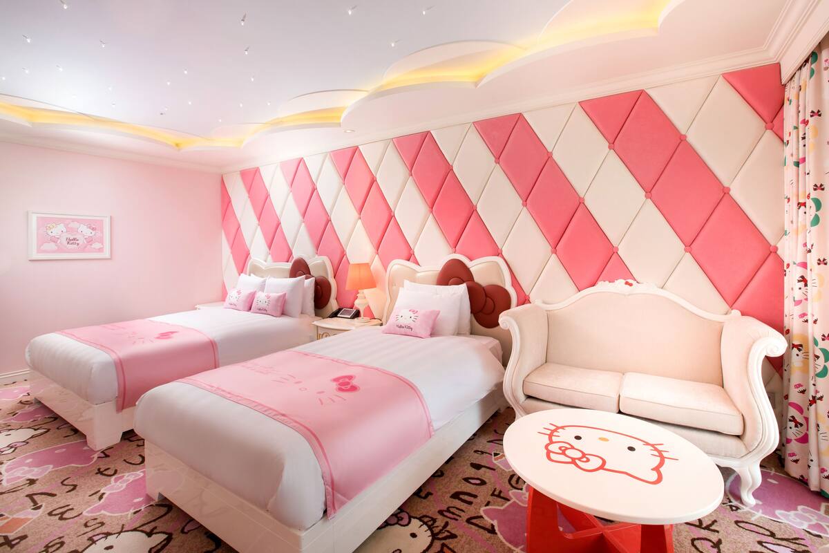 Une chambre d’hôtel décorée dans des tons roses, comprenant deux lits, un canapé, une petite table et un mur décoratif.