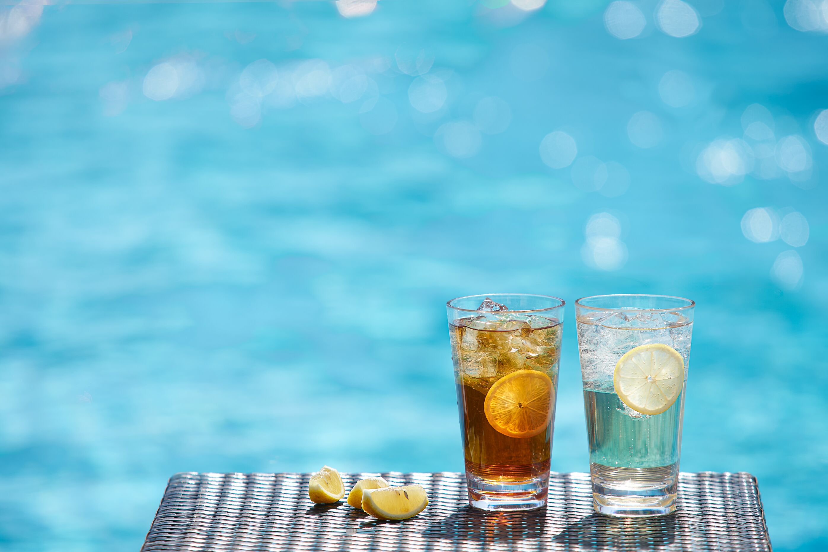 Two glasses of iced tea with lemon slices on a table by a pool.