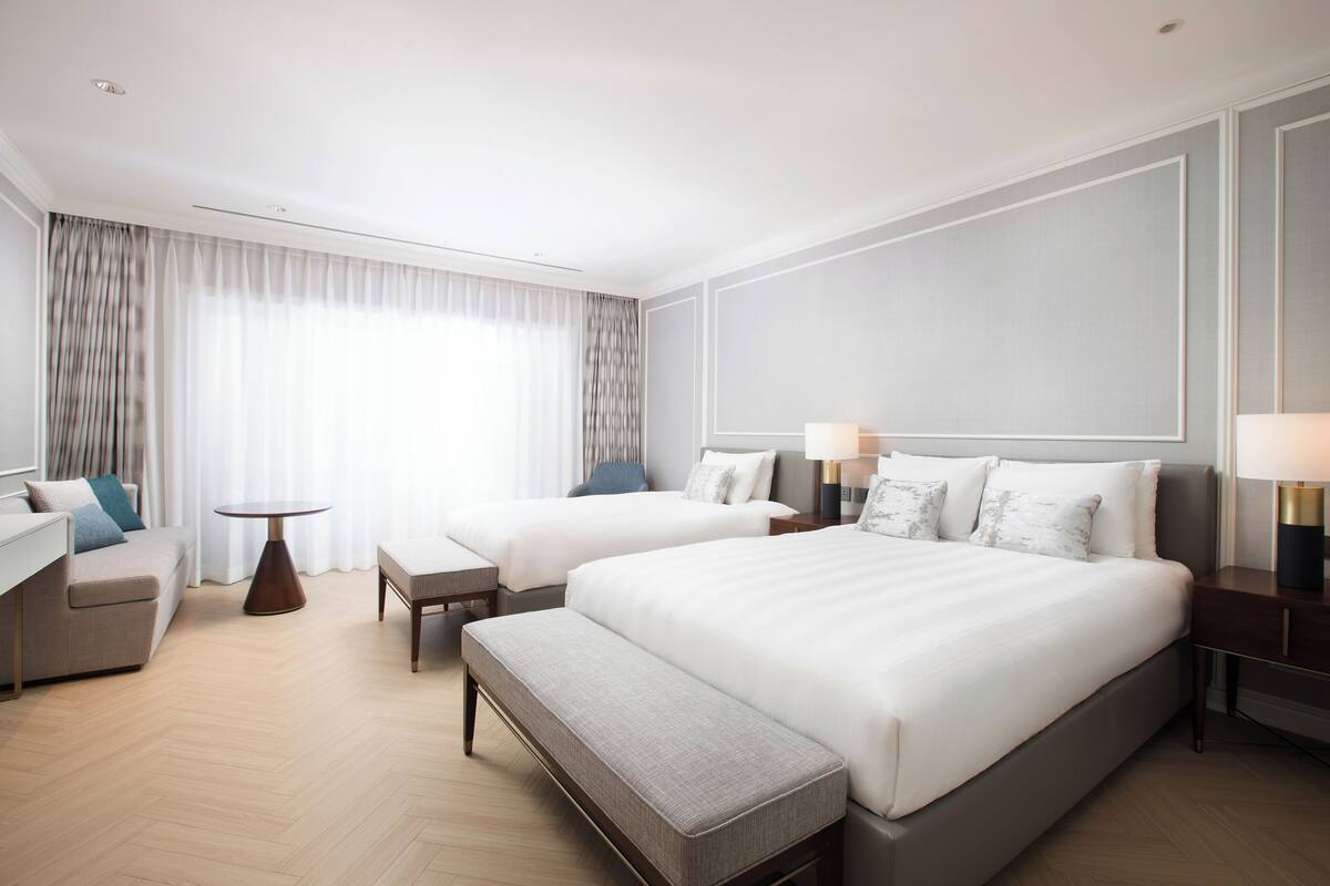 Une chambre d’hôtel avec deux lits, un canapé, une petite table et un banc.