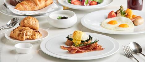 Desayuno con cruasanes, huevos y una variedad de frutas y verduras.