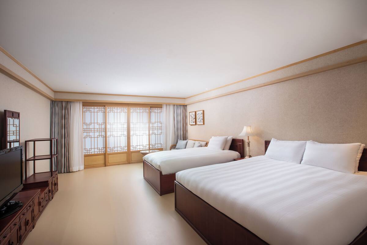 Une chambre d’hôtel avec deux lits, une télévision et une vue sur l’extérieur grâce à de grandes fenêtres.