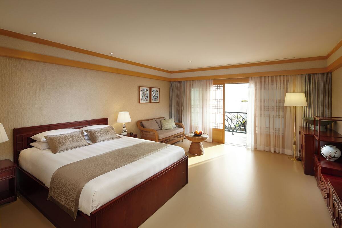 Une chambre d’hôtel avec un grand lit, un canapé, une petite table avec des fruits et une vue sur l’extérieur.