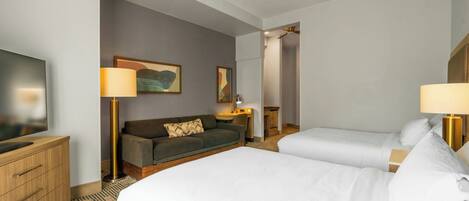 A hotel room with two beds, a sofa, a desk, a TV, and a painting on the wall.