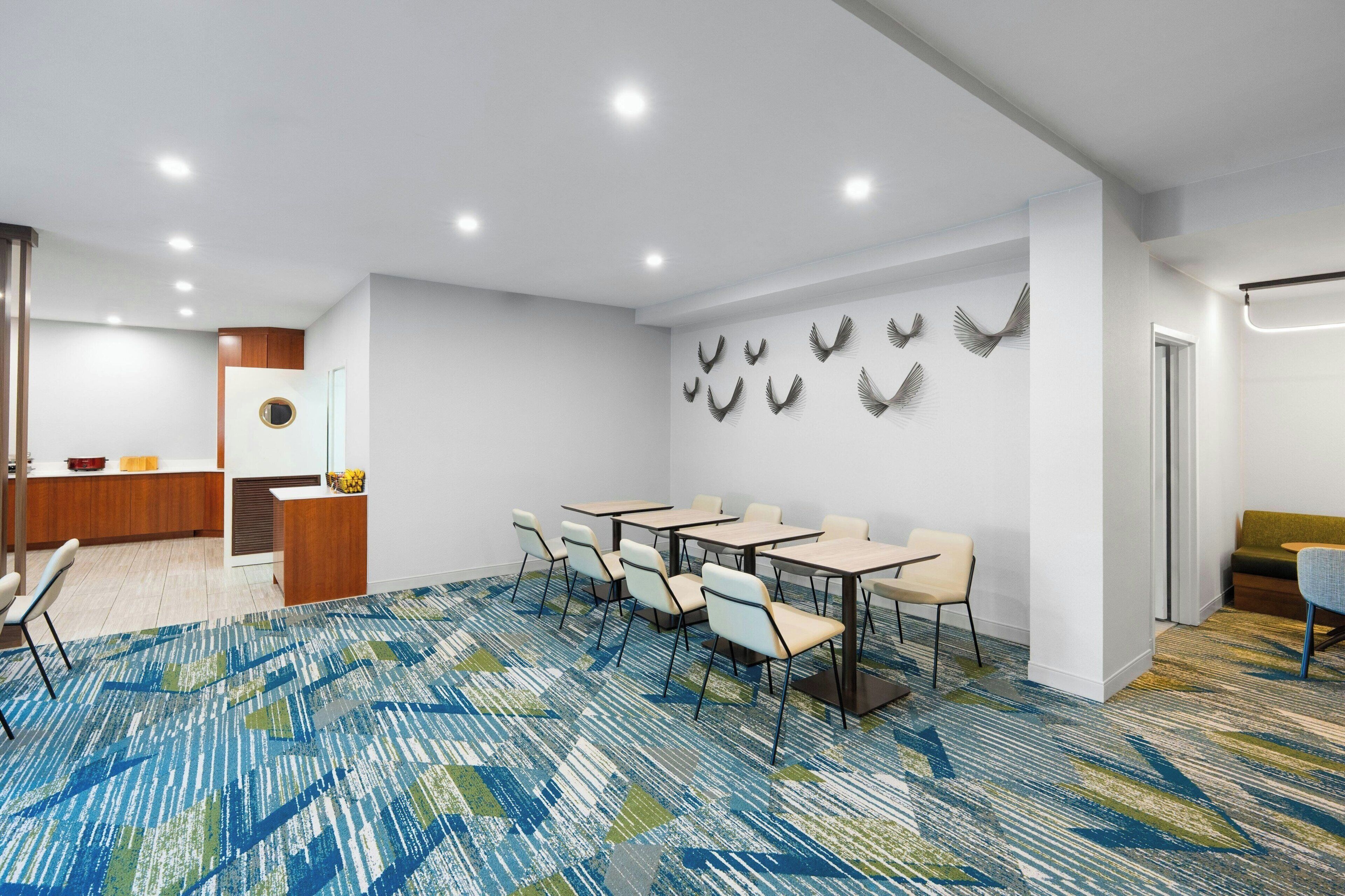 A conference room with a patterned carpet, white walls, and a row of tables with chairs.