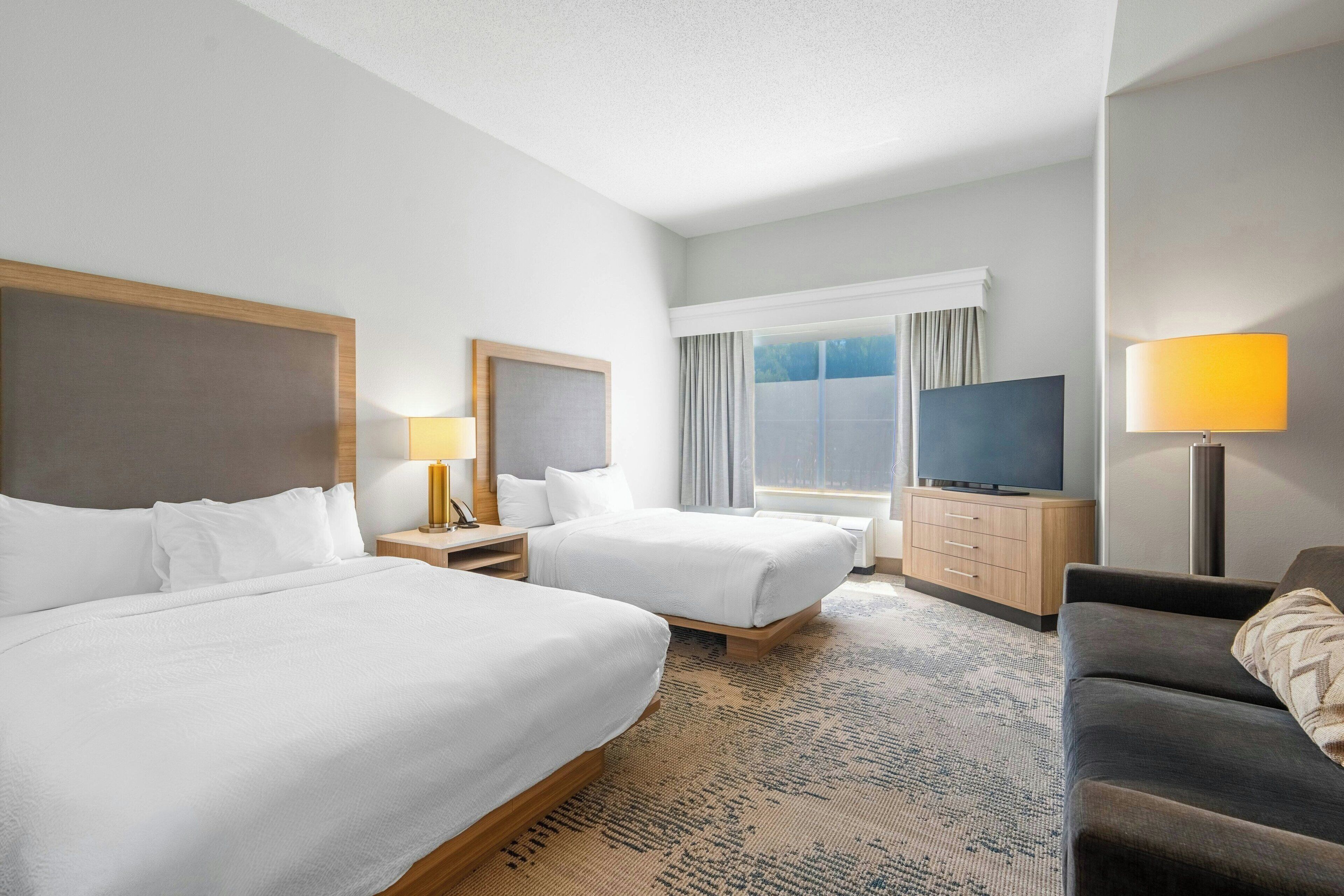 A hotel room with two beds, a sofa, a TV, and a window with curtains.