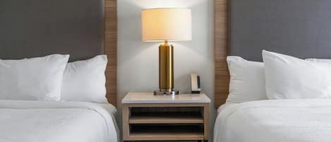 A hotel room with two beds, a nightstand with a lamp, and a patterned rug.