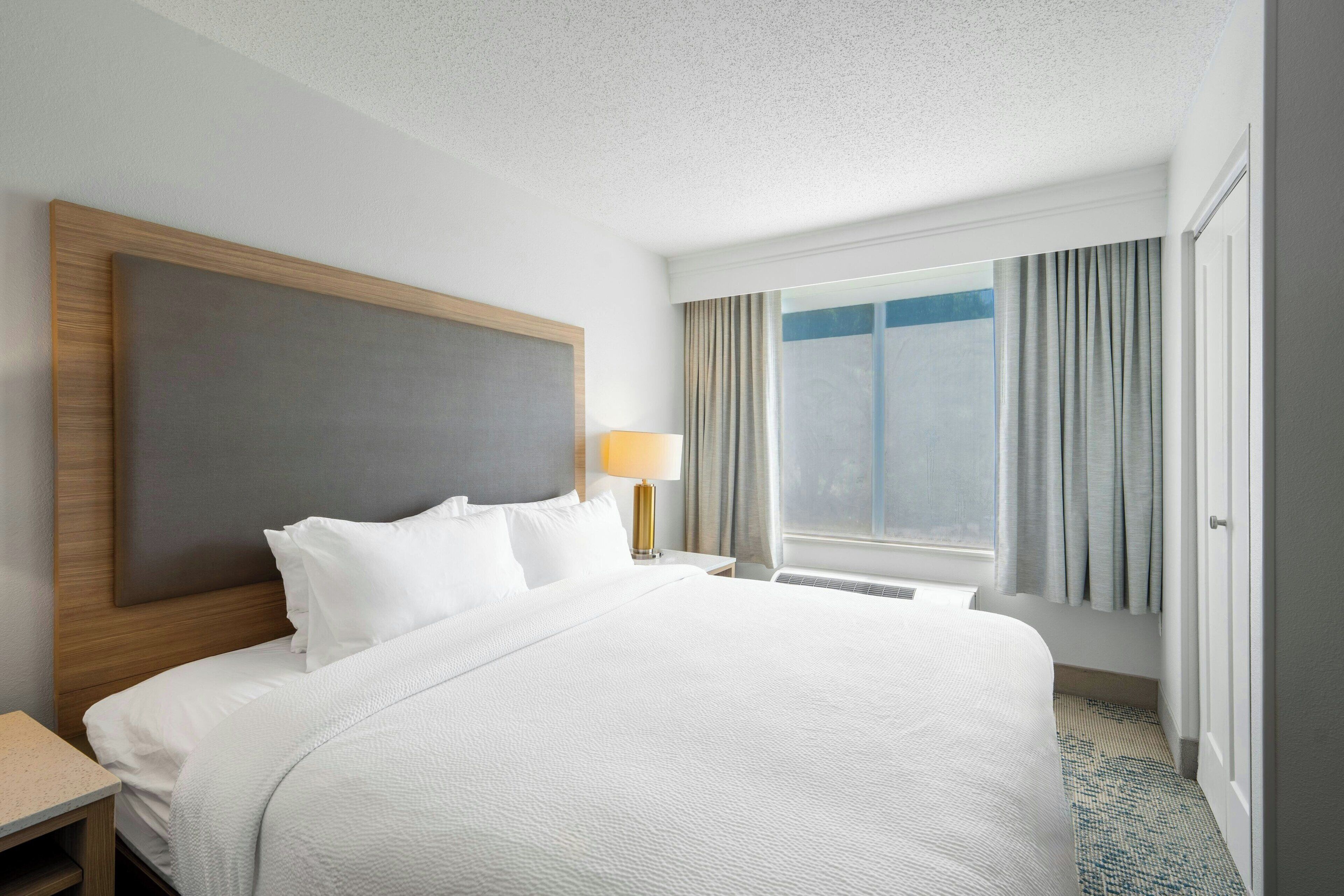 Una habitación de hotel con una cama grande, una mesita de noche, una lámpara y una ventana con cortinas.
